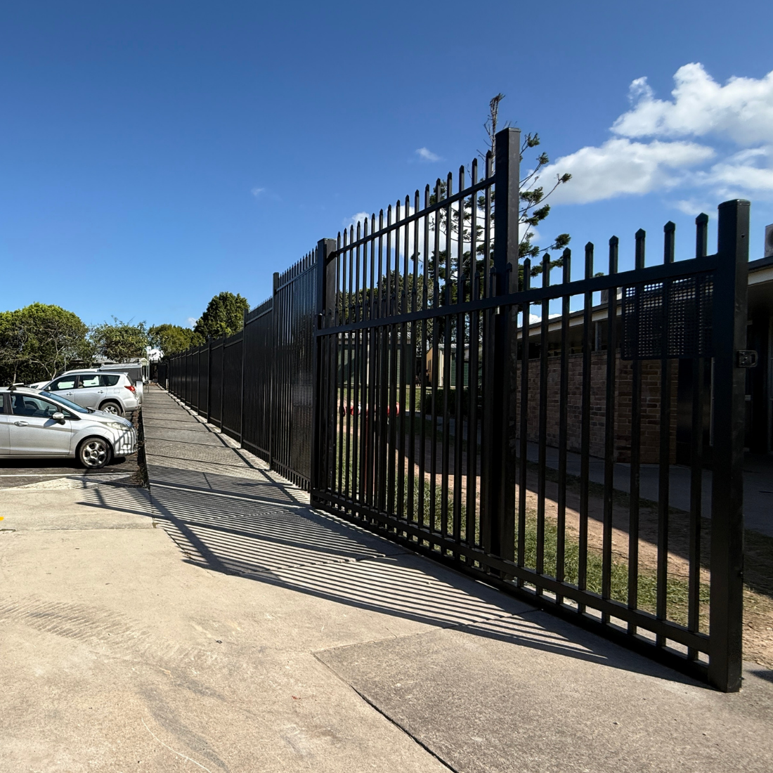 Black metal gate on a driveway with cars and trees in the background
