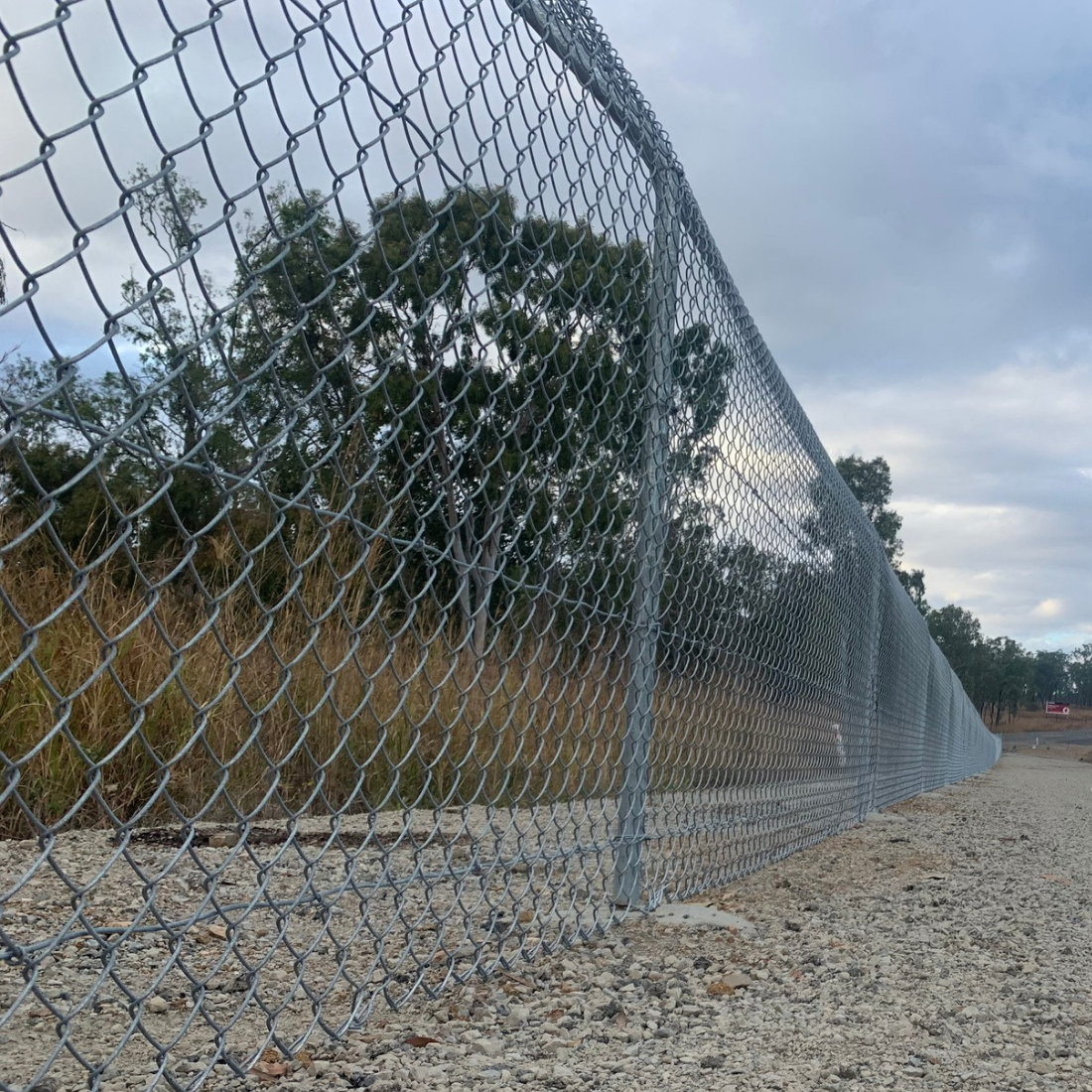 Chain-link fence with a gravel ground and trees in the background