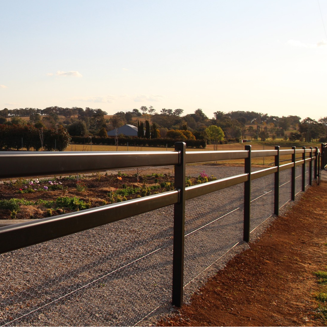 Fence line with a scenic view of trees and open field under a clear sky.